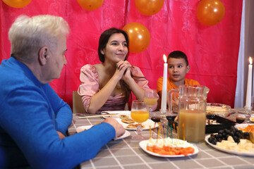 A girl with her family is sitting at the table and celebrating her birthday. Soft lighting.