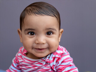 wonneproppen kleiner junge mit gro&szlig;en brauen augen und einem rot weiss gestreiften Strampelanzug der l&auml;chelnd in die Kamera schaut