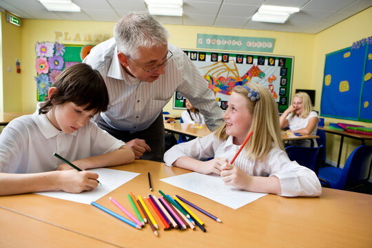 Junior School: Asking Teacher. A pair of young primary school children working in class on an art project while teacher offers some guidance.
