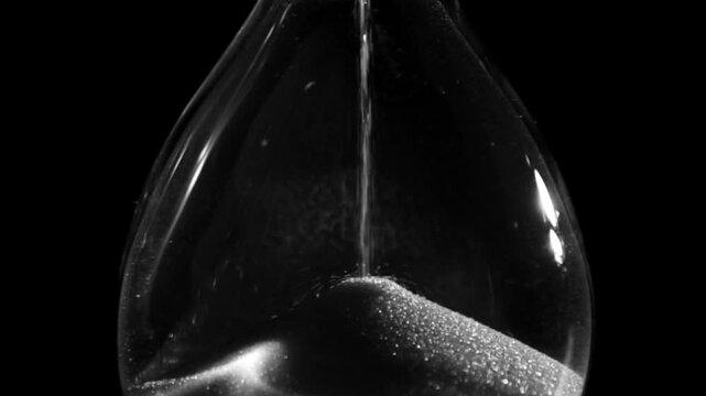 Black and white video slow motion of a hourglass: Sands move through hour glass. Close up video timelpase. Pass of time and  waste time concept