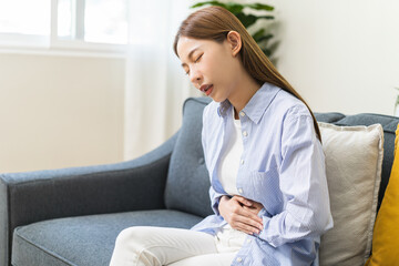Sick asian young woman in pain, hand holding belly, stomach pain from food poisoning, girl hurt...
