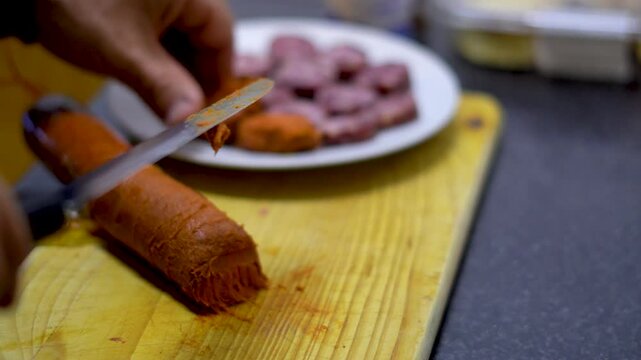 A person chops a sobrasada, on a wooden board, in the kitchen at home. Real time