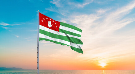 Waving flag of Abkhazia against the background of a sunset or sunrise. Abkhazia. sky with flying flag beauty.  Concept of national holidays. Flying Abkhazia National Flag for National Holidays.
