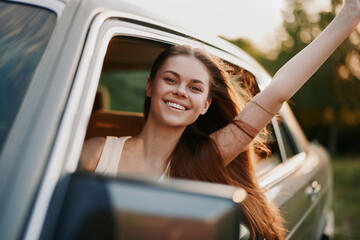 Young woman enjoying a road trip, smiling and waving from a car window, showcasing happiness and...