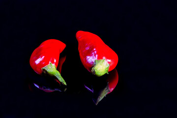 Two reshly harvested chili peppers displayed o a black surface