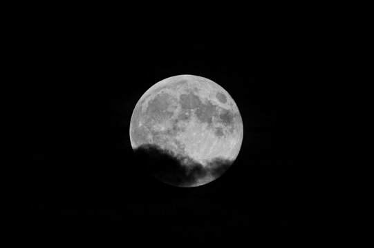 Close-up photo of the moon partially covered by clouds. Moon photo with black background. Cloudy photo of the moon.