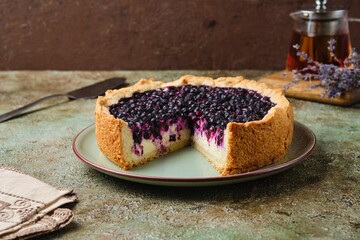 Round pie on shortcrust pastry with sweet curd filling and berries on a ceramic green plate on a green concrete background. Baking with cottage cheese.