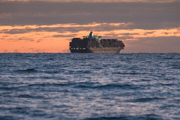Obraz premium sunset over the sea Cargo ship in the sea. A beautiful sunrise over the sea. Ship sailing along the sea horizon. Transport ship in the ocean. Sun reflections in the water