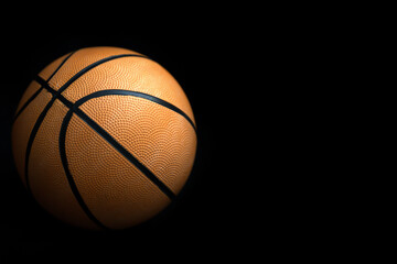 Basketball in orange color on a black surface isolated background with copy space on the side. Sports poster space design with basketball