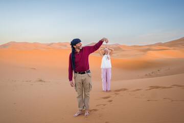 A couple plays at making optical illusions in the middle of the Sahara desert. It is sunset in the Sahara desert in Merzouga, Morocco