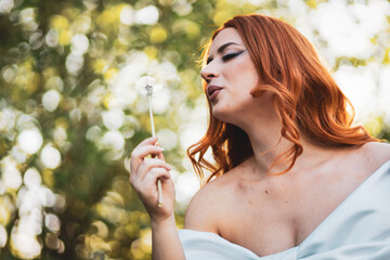 Young feminine girl in white dress blowing dandelion