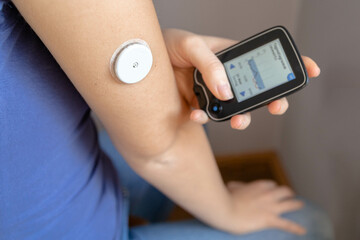 Girl sitting with sensor glucose patch on her arm looking at the monitor results