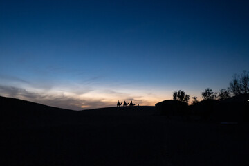 Fototapeta premium Stunning image in the Sahara desert at dusk. Three men ride camels towards a small camp. They look like the three wise men of the Catholic tradition at Christmas