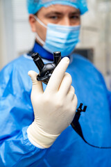 Surgeon shows instrument live. Medical professional in blue scrubs holds a surgical tool while...