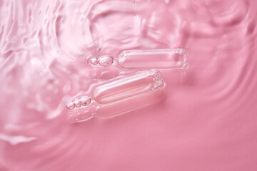 Ampoules in water on a pink background.
