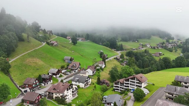 Drone flight above the village centre of Wildhaus, a charming village near the Alpstein mountain range. Small alpine town centre with church and houses. Surrounded with beautiful Swiss mountains. Clou