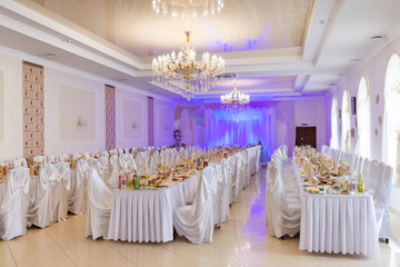 Chic banquet hall for events. A spacious banquet hall features elegantly set tables, decorative lights, and a grand chandelier, perfect for events.