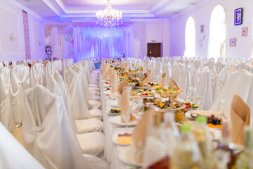 Chic banquet in a stylish hall. Long tables are beautifully arranged for a banquet with white tablecloths and an array of delicious dishes.