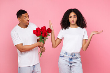 Young Latin woman ignore the apologize of her boyfriend, guy holding bouquet of red roses over pink...