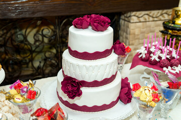 Elegant three-tier cake for celebration. A beautifully decorated three-tier cake adorned with deep red flowers, set up for a festive celebration.