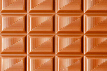 A close up of a chocolate bar with brown squares. The chocolate bar is brown and has a rectangular...