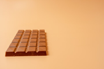 Chocolate on an orange background. A chocolate bar is cut in half and lies on the table.