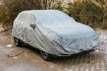 Vehicle covered with a protective tarp in a snowy neighborhood