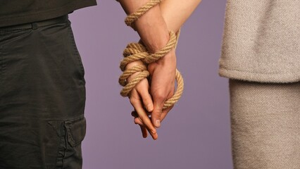 Man and woman holding hands tied together, tangled with rope, abusive unhealthy codependent...
