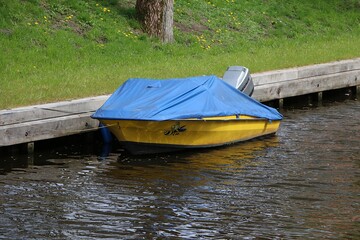 small cute yellow boat lies on the bank of a small river covered with a blue tarpaulin