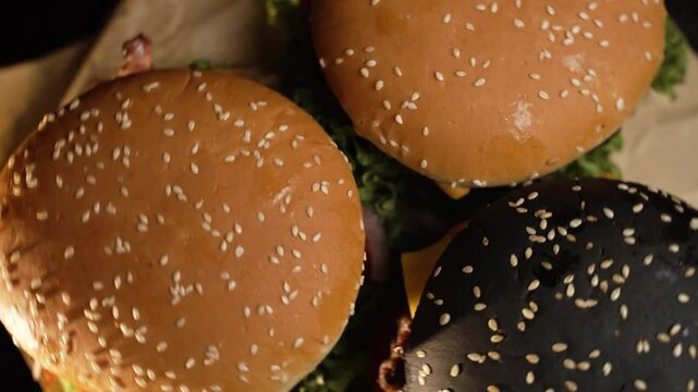 Three juicy fresh burgers with sesame seed buns, vegetables and meat slowly rotate on the table