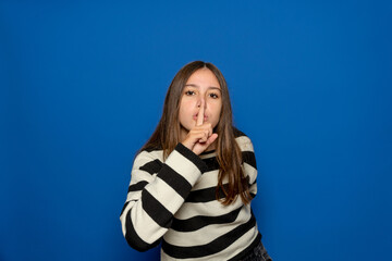 Teenage girl presses index finger to lips and makes a hush gesture to not tell secrets and stop...