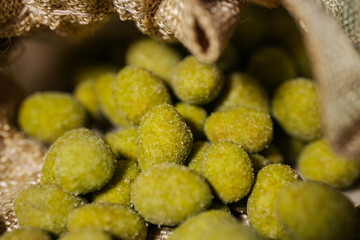 Close-up of vibrant yellow-green wasabi-coated nuts spilling out of a rustic burlap sack. Coated in a fine powder, they appear crunchy and flavorful.
