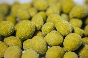 A close-up view of bright yellow-green wasabi-flavored nuts coated in a fine powder, creating a spicy and crunchy snack. Blurred background for emphasis.