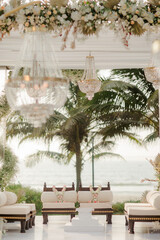 A romantic white beach wedding celebration with an outdoor ceremony, featuring elegant decor, a bottle for colored sand rituals, and a beautifully arranged table under the open sky