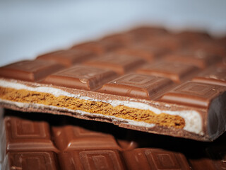 A close-up of a milk chocolate bar, showing a crispy layered filling of golden biscuit and creamy white chocolate against a soft fabric background.