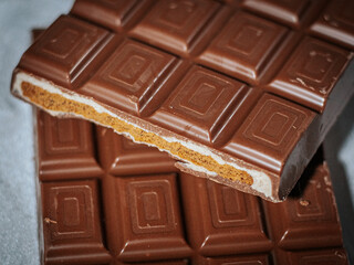 A close-up of a milk chocolate bar, showing a crispy layered filling of golden biscuit and creamy white chocolate against a soft fabric background.