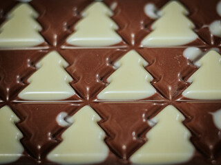 A close-up of a holiday chocolate bar with tree-shaped milk and white chocolate patterns showcasing the textures of a fir tree and the holiday theme.