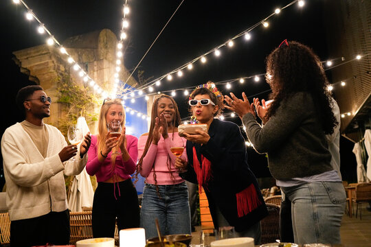 Multiethnic friends celebrating birthday party at night with cake and drinks