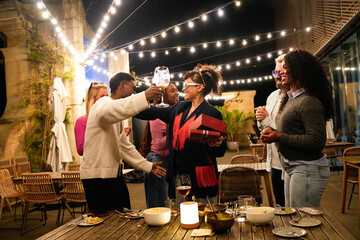 Friends celebrating birthday party at night, toasting with wine outdoors