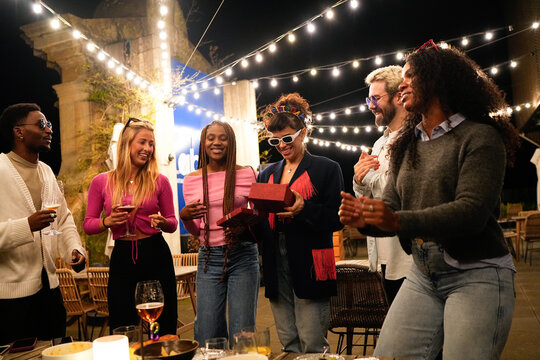 Happy multiethnic friends celebrating outdoors, giving gifts at night party