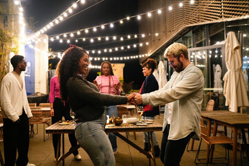 Friends dancing together at rooftop party under string lights