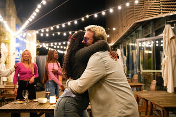 Multiethnic friends hugging at outdoor party with string lights