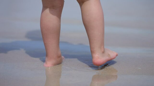 Toddler taking first steps on wet sand at beach
