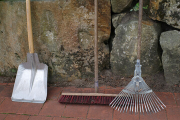 Garden tools standing against an old wall. These are tools to collect leaves: shovel, broom and...