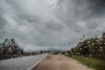 Raindrops on Windshield with a Blurred Countryside Road Under Cloudy Skies