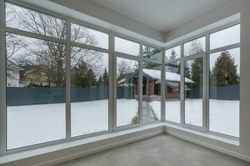 Snow-covered courtyard of a country house from a panoramic window of a room with modern renovation , unfurnished.