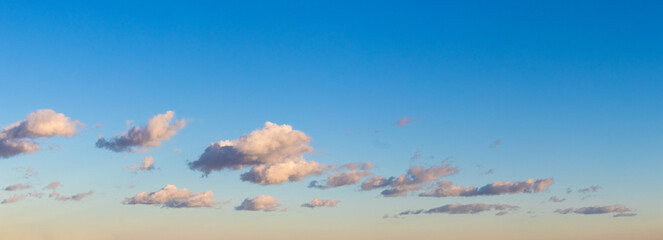 small curly clouds lined up in a row in the blue sky