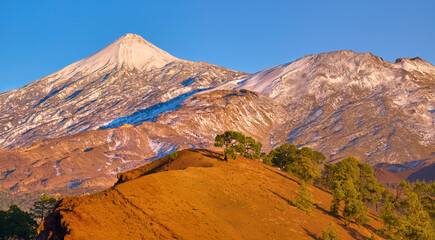 Aerial, panoramic  view of Mount Teide volcano, covered with snow, pinkly illuminated by the setting sun. A vibrant landscape in Tenerife, Canary Islands. Ideal for travel, nature and adventure.