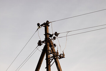 Close-up of the top part of an electric pole with power lines stretching across the sky. A clear view of the cables and pole structure, showcasing industrial energy infrastructure against a blue sky