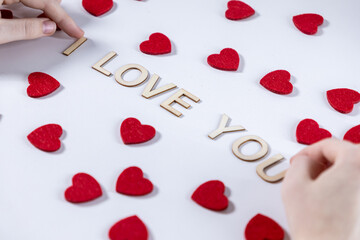 person arranging wooden letters to spell i love you on a white background surrounded by scattered red felt hearts symbolizing romance and Valentine's Day